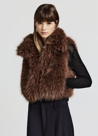 Braune Fake-Fur-Weste mit breitem Kragen, die eine lange, flauschige Textur aufweist. Kombiniert mit einem schwarzen, gerippten Langarmshirt und tailored schwarzen Hosen.