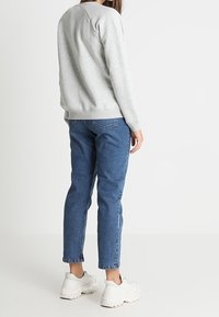 Grå sweatshirt med ribbade manschetter och avslut, matchad med blå jeans som har rak passform och något avsmalnande ben. Vita sneakers fulländar looken.