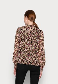 Blusa nera con motivo floreale multicolore, dettaglio cut-out sul retro, maniche lunghe con polsini arricciati e tessuto leggero e trasparente.