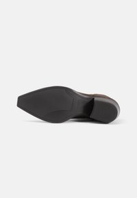 Brown suede shoe sole with a sleek design, featuring a rubberized grip and a pointed toe shape. Imprinted brand logo near the heel.