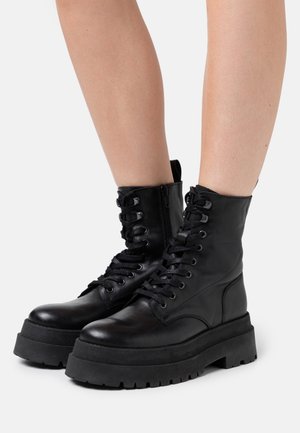 Legs wearing black high-top lace-up platform boots with thick soles, smooth leather texture, and side zippers, against a white background.