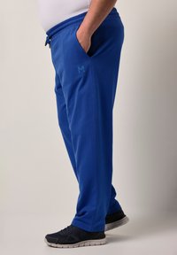 Blå sweatpants med elastiskt midjeband, sidofickor och en liten logotyp på vänster lår. Har en avslappnad passform och en mjuk textur.