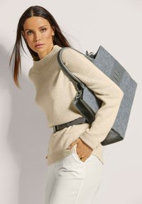 Beige Strickpullover mit hohem Kragen, graue Filztasche, weiße Hose und grauer Gürtel. Glatte Textur, klare Linien und funktionales Design.