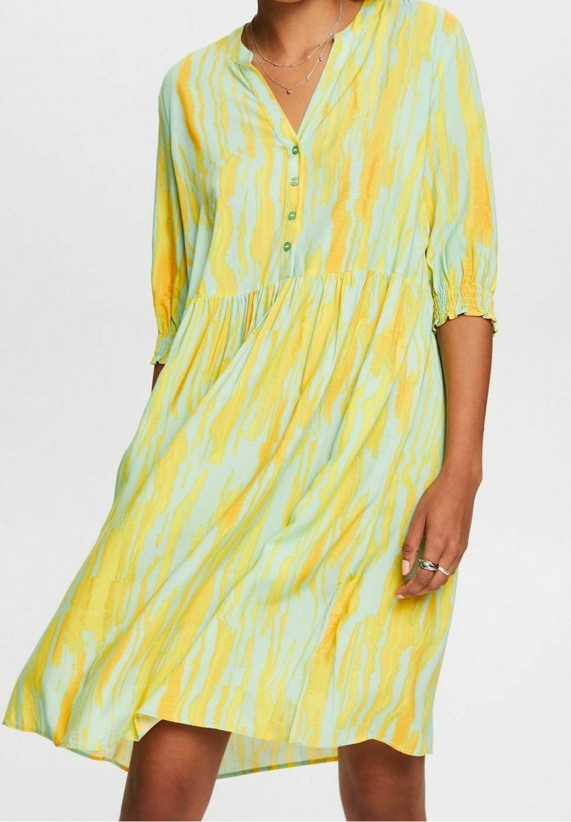 Robe légère et fluide en vert menthe avec des rayures jaunes. Présente un décolleté en V, une fermeture à boutons et des manches trois-quarts avec des poignets froncés.