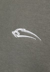 Olivenfarvet stof med en tekstureret finish, der har et fremtrædende hvidt broderet logo design.