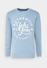 Sudadera azul claro hecha de tela suave, con un logo circular blanco que presenta el texto "AUTHENTIC Jack & Jones DENIM CO SINCE 1990."