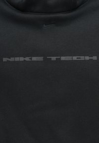 Fekete Nike Tech pulóver, sima szövettextúrával, lekerekített nyakkivágással és egy nagy, struktúrált "NIKE TECH" logóval az elején.