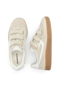 Baskets en daim beige avec trois bandes Velcro, accents blancs et semelles en caoutchouc présentant une surface texturée. Marque visible à l'intérieur de la chaussure.