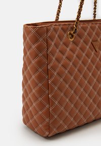 Borsa tote sintetica marrone trapuntata con cuciture bianche, dotata di un accento a logo triangolare e manici in catena dorata.