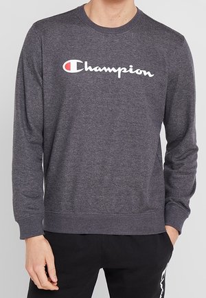 Sweatshirt gris à col rond en tissu doux avec un logo "Champion" blanc bien visible. Les poignets et l'ourlet à côtes complètent le design.