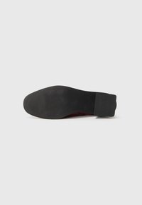 Suola in gomma nera di una scarpa elegante con un tacco liscio e un'area di presa testurizzata, mostrata dal basso su uno sfondo bianco uniforme.