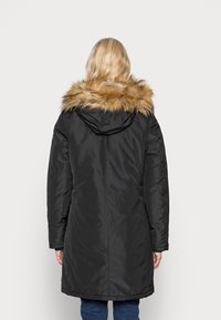 Veste en doudoune noire avec un col à fourrure synthétique, design mi-long et manches longues. Texture lisse avec un détail fonctionnel à l'arrière.
