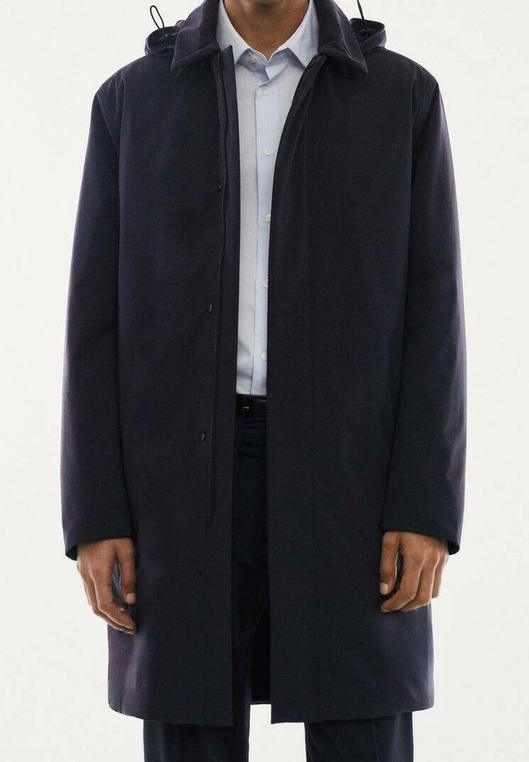 Abrigo azul marino con capucha, con corte recto, cierre de botones de presión y mangas largas. Fabricado con una tela lisa, se lleva sobre una camisa ligera.