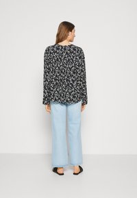 Svart langermet bluse med hvitt blomstermønster, avslappet passform. Kombinert med lyseblå vide jeans og svarte slip-on sko.