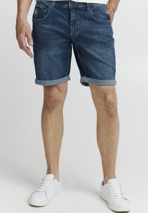 Shorts di jeans di colore blu scuro, con orli risvoltati, cinque tasche e un leggero effetto scolorito. Abbinati a sneakers bianche.