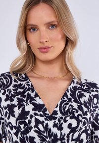 Navy and white patterned wrap dress with short sleeves and a v-neckline, featuring a smooth fabric and a gold necklace as an accessory.