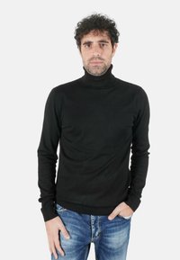 Maglione dolcevita nero in materiale morbido, con maniche lunghe e design aderente, abbinato a jeans di denim blu.
