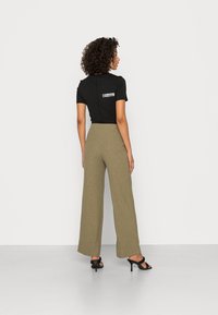 Top preto de mangas curtas com detalhe gráfico branco, combinado com calças em rim olive de perna larga. Usado com saltos abertos pretos.