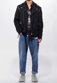 Černá koženková motorkářská bunda se stříbrnými zipy, přes šedou kostkovanou košili. Volné modré džínové kalhoty a světle šedé tenisky dokončují vzhled.