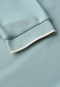 Tissu bleu clair avec une texture lisse, présentant un poignet avec un accent blanc. Matériau doux et extensible, adapté aux vêtements de sport.