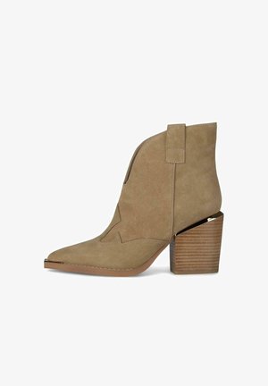 Beige suède enkellaars met puntige neus, blokhouten hak en decoratieve stiksels aan de zijkant en voorkant.