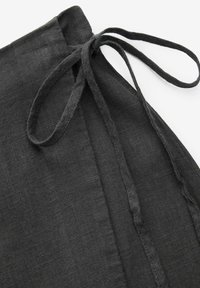Black linen garment with a tie closure at the waist, featuring a textured fabric and a smooth drape. Simple, minimal design.