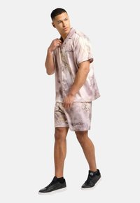 Kortærmet pastelrosa skjorte og matchende shorts med snoede mønstre og brandlogo. Båret med sorte sneakers. Glat stofstruktur.