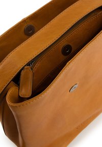 Sac à main en cuir tan avec fermeture éclair, texture lisse et accents métalliques, doté d'une poche à pression à l'avant. L'intérieur est doublé de tissu.