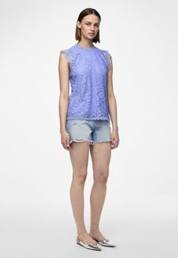 Lilla blonde topp med scalloped halskant og cap-sleeves, sammen med slitte denimshorts og metalliske slip-on sko.