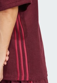 Camiseta deportiva color burdeos con una tela texturizada, de mangas cortas y tres rayas verticales rosas a lo largo del costado.