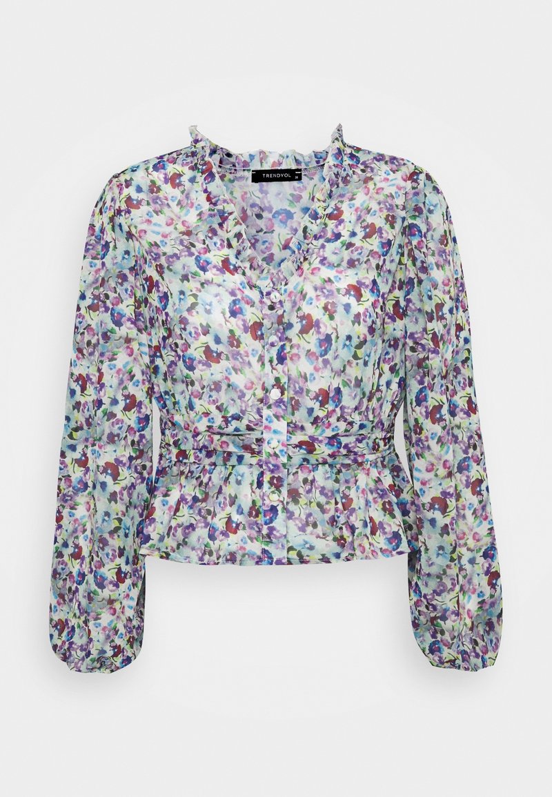Blouse fleurie en tissu léger et transparent. Elle présente des manches longues, un col à volants, une patte de boutonnage à l'avant et une taille peplum. Les couleurs incluent le violet, le bleu et le vert.