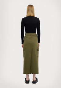 Gonna midi in cotone verde con due tasche cargo laterali, abbinata a un top fitted a maniche lunghe nero e calzature nere texturizzate.