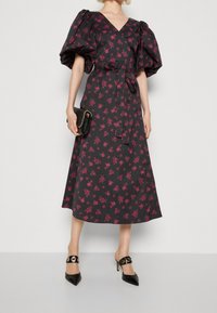 Vestido negro con estampado floral y mangas abullonadas, con escote en V y cintura con lazo. Combinado con mules negras con detalles en dorado.