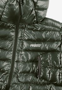 Zielona kurtka puchowa o błyszczącym wykończeniu, z zamkiem błyskawicznym, kapturem oraz zapinaną na zamek kieszenią na piersi. Tkanina ma pikowany wzór.