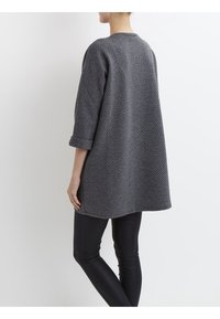 Grå stickad tunika med ett texturerat mönster, rund halsringning, trekvartsärmar och en lös passform, tillsammans med svarta leggings.