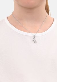 Collana d'argento con un pendente di unicorno dettagliato, indossata su una semplice camicia bianca. La catena è fine e metallica, in perfetta armonia con il pendente.