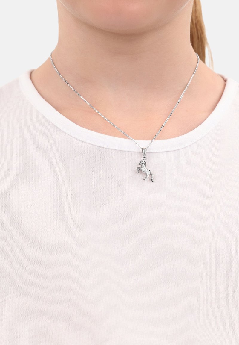 Collana d'argento con un pendente di unicorno dettagliato, indossata su una semplice camicia bianca. La catena è fine e metallica, in perfetta armonia con il pendente.