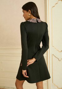 Čierne šaty s priliehavým strihom, dlhými rukávmi a golierom s leopardím vzorom. Hladká látka s dĺžkou siahajúcou po kolená.