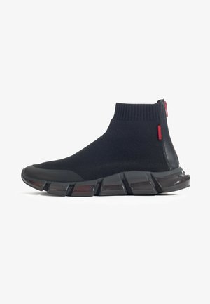 Zapatilla negra tipo calcetín de caña alta con tobillo de punto acanalado, suela segmentada y gruesa, cremallera roja y pequeña etiqueta roja en el lateral.
