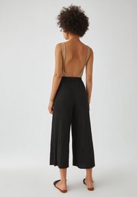 Des culottes longues noires texturées associées à un top beige sans dos. La tenue présente des jambes larges et une coupe décontractée avec un design simple.