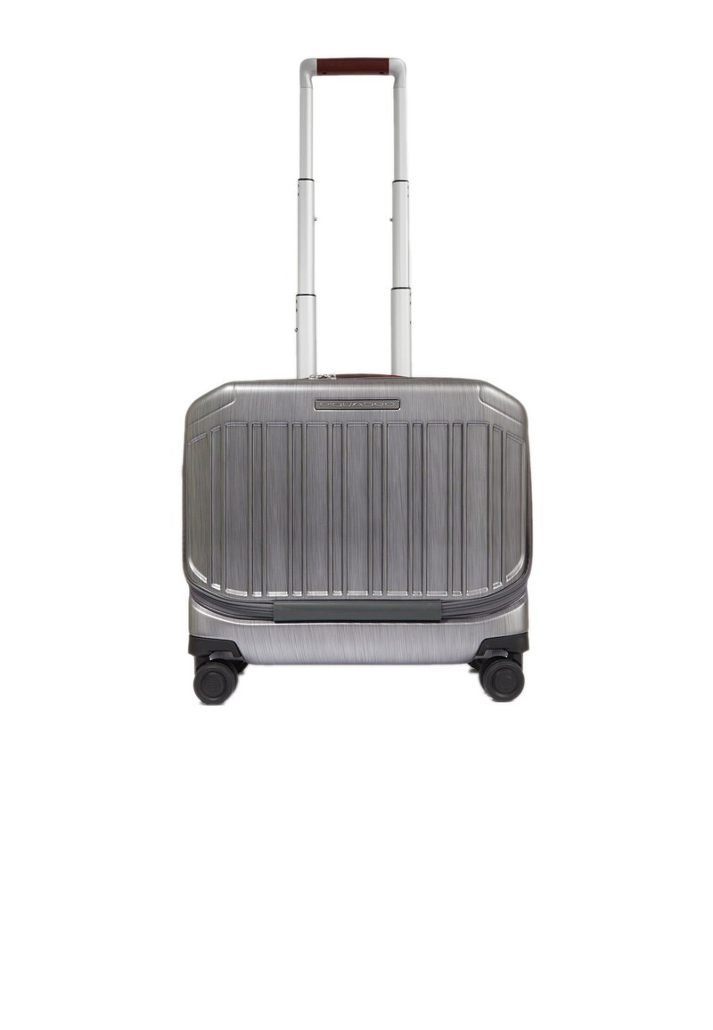 Zilverkleurige harde koffer met verticale ribbels, telescopisch handvat en vier wielen voor mobiliteit; voorzien van een bruine lederen accenten op het handvat.