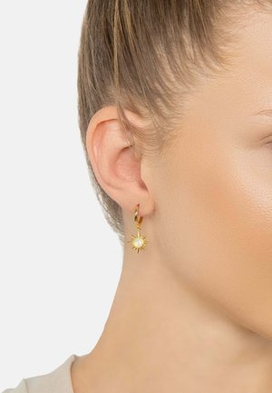 Gold hoop earrings featuring a sun-shaped charm with a central white stone. The charm has pointed rays extending from the center.