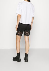 White cropped t-shirt, black lace shorts with scalloped hem, paired with black chunky boots. Focus on material contrast and layered textures.