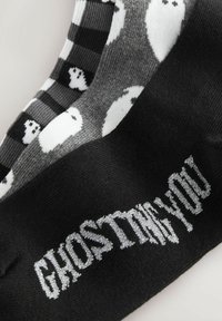 Crne čarape s ljubičastim natpisom "GHOSTING YOU." Sivi i crni prugasti dizajn s bijelim uzorkom duhova. Mekana tekstura tkanine.