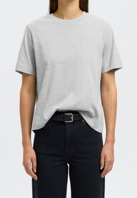 Hellgraues Baumwoll-T-Shirt mit klassischem Rundhalsausschnitt und kurzen Ärmeln, kombiniert mit schwarzen, hochgeschnittenen Jeans und einem schwarzen Gürtel.