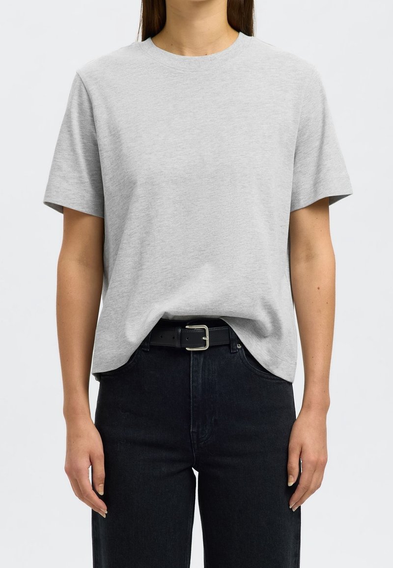 Hellgraues Baumwoll-T-Shirt mit klassischem Rundhalsausschnitt und kurzen Ärmeln, kombiniert mit schwarzen, hochgeschnittenen Jeans und einem schwarzen Gürtel.