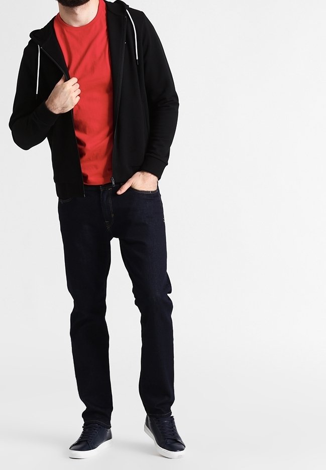Sudadera negra con cremallera y cordones blancos, camiseta roja debajo, jeans azul oscuro y zapatillas azules. Un atuendo sencillo y casual.