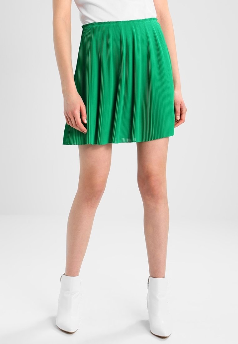 Groene geplooide rok met een aangesloten taille en vloeiende vorm, gemaakt van lichte stof, gecombineerd met witte enkellaarsjes.