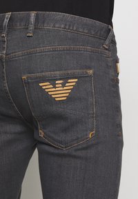 Dark denim jeans with orange stitching and a distinctive logo on the back pocket. The fit is slim, with standard pockets and mid-rise waist.