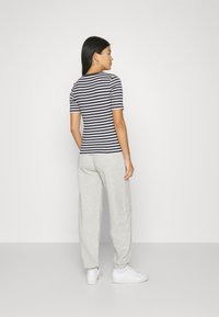 Camisa de rayas de manga corta, con un patrón azul marino y blanco, combinada con pantalones de chándal grises claros; zapatillas blancas en los pies.
